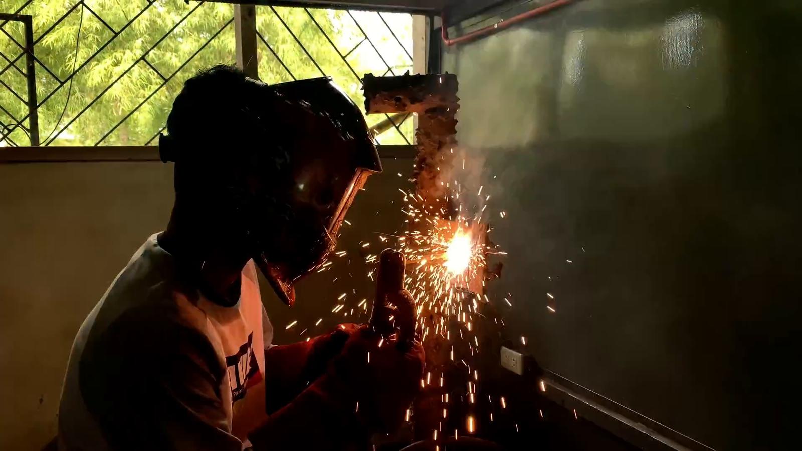 A welder at work behind a mask, sparks flying from the metal.
